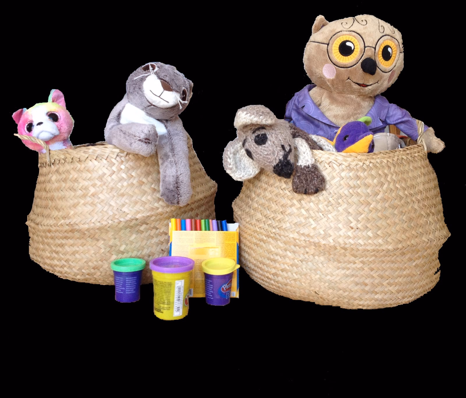 Deux grands paniers en osier remplis de peluches (un chat, un koala, une chouette à lunettes) posés au sol, avec des pots de pâte à modeler et une boîte de feutres.